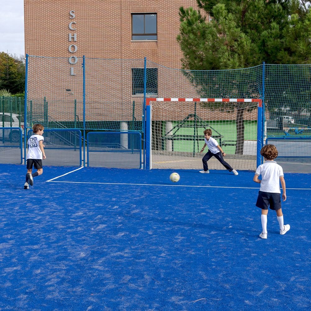 Niños practicando deporte en la pista exterior azul del colegio Highlands en El Encinar, zona residencial cercana a La Moraleja.