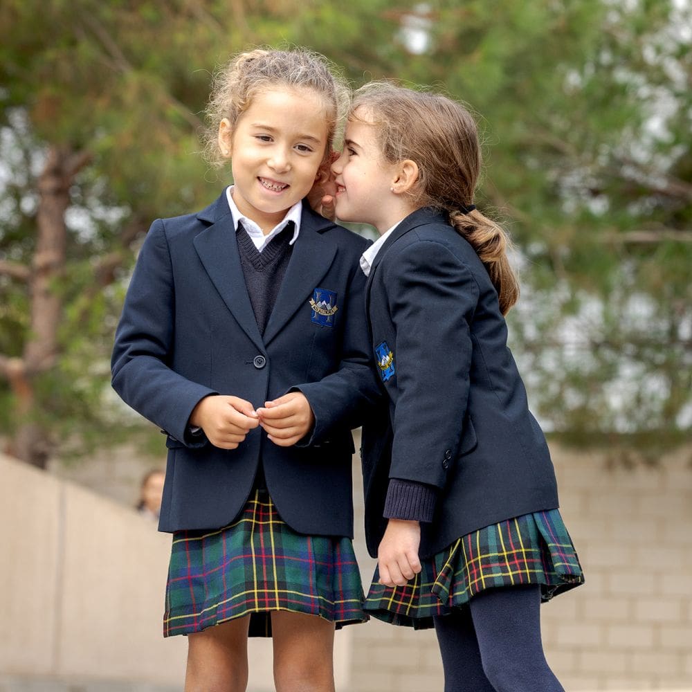 Dos alumnas de infantil del colegio Highlands en El Encinar posando con uniforme escolar en un entorno natural cercano a La Moraleja.