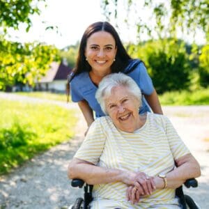 Cuidadora asistiendo a mujer mayor en silla de ruedas en jardín de urbanización en La Moraleja, Madrid.