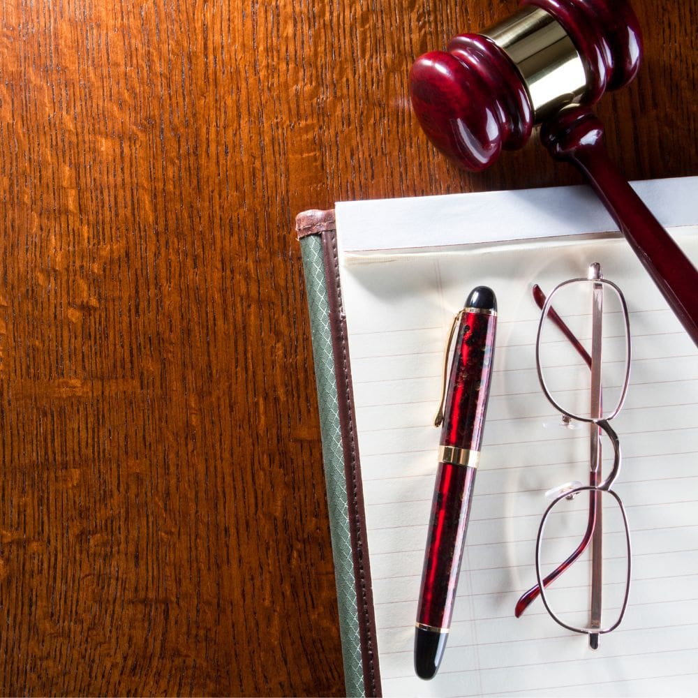 Primer plano de un mazo de juez de madera noble, una pluma estilográfica y gafas sobre un bloc de notas en un despacho de abogados de lujo en La Moraleja.